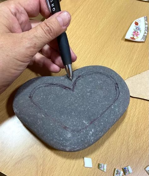 After a beautiful walk on holiday along a pretty cobbled beach, I just fell I love with the variety of ancient smooth sea washed stones . I stumbled across a sort of heart shaped one and decided to try creating unique mosaic on it using vintage crockery. I begin by drawing a heart shape onto the surface of stone with a pen. This gives a rough outline to work within. I use wheeled tile nippers to break up some old ceramic saucers and cups and find the little floral designs for my he… Drawing A Heart, Heart Shaped Rocks, Heart Rocks, Black Grout, Mosaic Rocks, Vintage Crockery, Mosaic Tile Art, Stone Crafts, Mosaic Stone