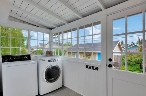 This mudroom or sun porch is at the back of an old Tacoma Craftsman home and is classically charming with its paned windows and white paint. There's room for laundry, workspace, and storage, but I'd be tempted to set up the wicker chair and cushions back there.   #mudroom #sunporch #craftsmanhome #dugganhomes #laundryroom #backporch #enclosedporch Laundry Room On Sun Porch, Laundry Room On Porch, Laundry Room With Lots Of Windows, Laundry Porch Ideas, Porch Laundry Room Ideas, Back Porch Mudroom Ideas, Laundry On Deck, Screen Porch Mudroom, Back Porch Laundry Room Ideas