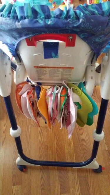 Easy and free storage solution for bibs. I saw on Pinterest many pins about command hooks and strips to hang up bibs on the back of your baby's highchair, however I noticed that the hooks only hold so many bibs. Since we go through a lot of bibs in a day, I needed a better solution. Our high chair has a bar in the back in which I was able to store all of Cookie's bibs for free! no hooks needed.  ~Lorelei Ns How To Store Bibs, Baby Highchair Storage, Pushchair Storage, Baby Hat Storage, Bib Storage Ideas, Baby Food Storage Organization, Bib Organization, Hanging Pacifier Storage, Bib Storage