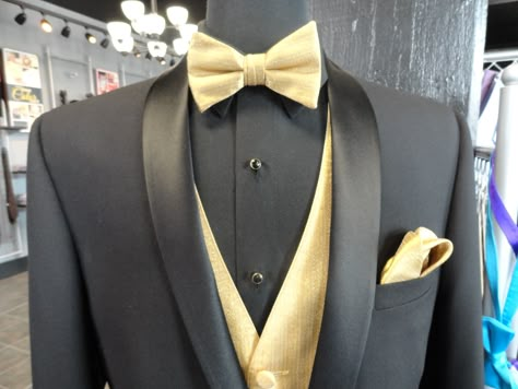 Be ready to steal any Belle away from the ball with this Black David Tutera tuxedo with our metallic gold bowtie, vest and pocket square combination. Black Tux Gold Vest And Tie, Tuxedo With Gold Accents, Black And Gold Tuxedo Men, Champagne And Black Suits For Men, Black White And Gold Mens Suit, Black And Gold Groomsmen Suits, Men Black And Gold Suit, Black Tux Gold Tie, Gold Suits For Men Wedding Ideas