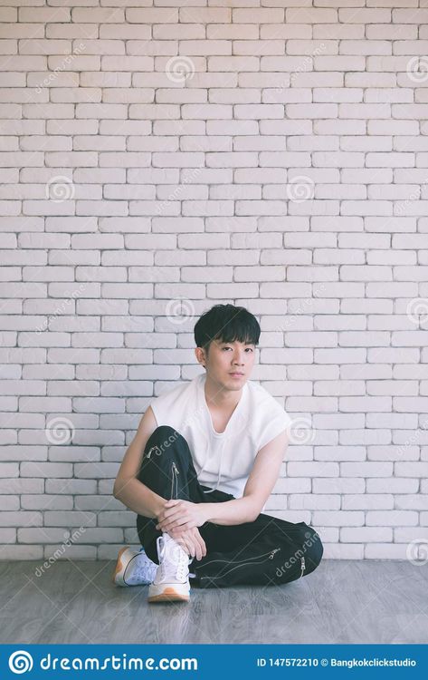 Photo about Asian model man in black pants and white shirt sitting on floor and knee up, photo shot on white bricks wall background. Image of adult, concept, asia - 147572210 Man Sitting On Floor Pose Reference, Guy Sitting Side View, Sitting Reference Pose Floor, Guy Sitting On Floor, Dynamic Sitting Poses, Body Reference Sitting, Man Sitting On Floor, Sitting Photography, White Bricks