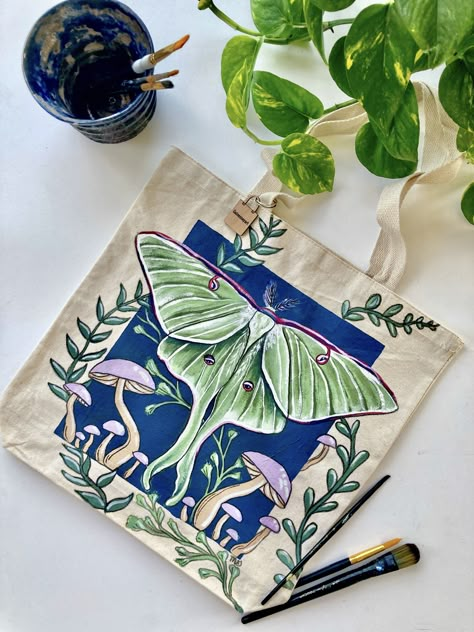 This is a green luna moth hand-painted tote bag with a navy blue background and purple mushrooms. Luna Moth Painting, Moth And Mushroom, Luna Moth Design, Diy Bag Painting, Moth Painting, Mushroom Tote Bag, Diy Tote Bag Design, Painted Canvas Bags, Moth Design