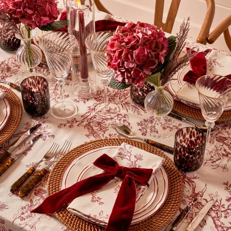 Add gold candle holders with white or red candles to create a warm, glowing ambiance. Burgundy Plate Setting, Christmas Table Settings Red Plates, Red Thanksgiving Table, Burgundy Christmas Tablescape, Simple Christmas Place Settings, Christmas Table Settings Round Tables, Red Table Cloth Christmas, Thanksgiving Plate Setting, Christmas Dinner Table Settings Elegant