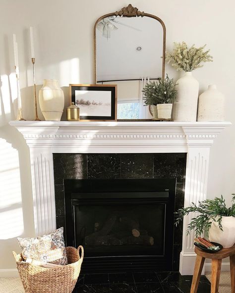 Neutral decor, such as the brass mirror and wooden photo frame, add a slight color accent to this monochrome white and black living room. The white stone vases on the mantel create an elegant, seamless look that blends perfectly with the white walls and mantel. Elevate the decor with gold-plated candle holders for a timeless aesthetic. Mantel Decorating Ideas Picture Frames, White Tv Mantle, Styling Mantle With Mirror, White Fireplace Mantels Decor, Mantel Photo Display, Mantel Decorating Ideas With Pictures, White Fireplace Mantle Decor, White Mantle Decorating Ideas, White Mantel Decorating Ideas