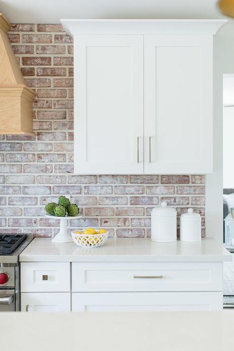 White shaker kitchen cabinets feature nickel knobs, white quartz countertops, and red brick backsplash tiles. White Kitchen With Brick, Red Brick Kitchen, Backsplash Kitchen White Cabinets, Brick Kitchen Backsplash, White Quartz Countertops, Brick Backsplash Kitchen, White Shaker Kitchen Cabinets, White Shaker Kitchen, Brick Kitchen