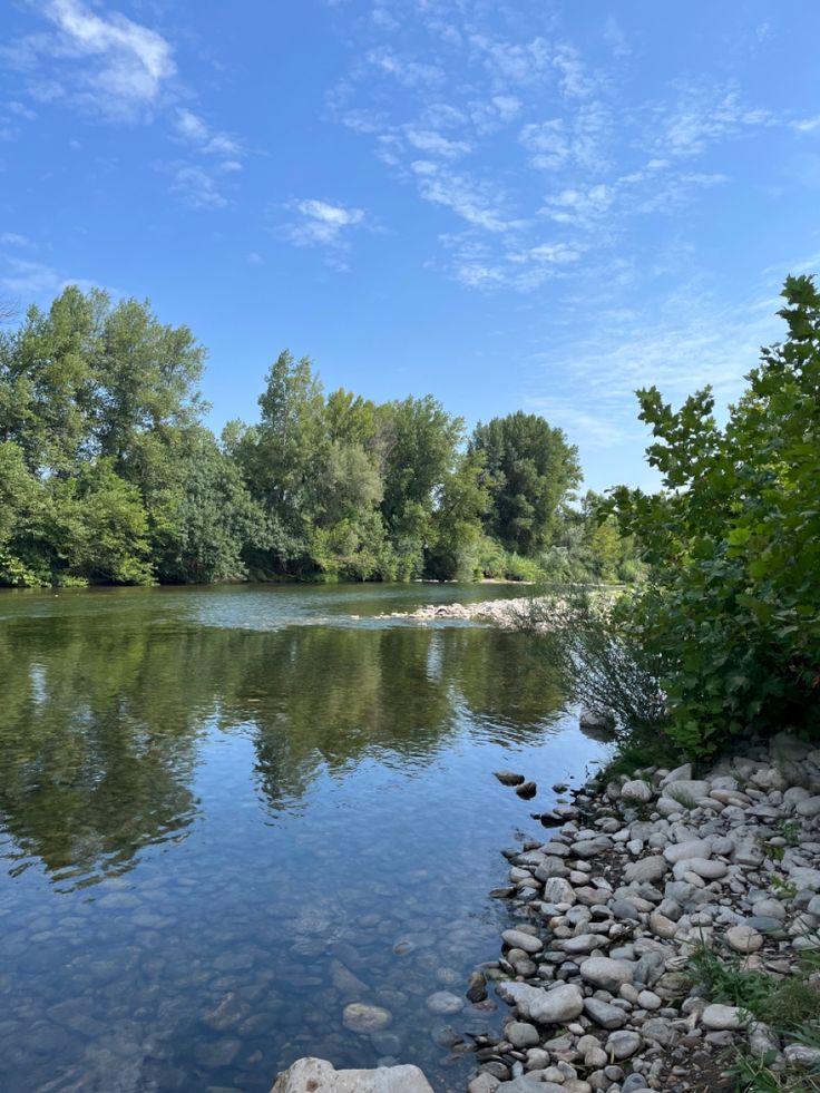 a river with rocks and trees on both sides, under a blue sky filled with clouds