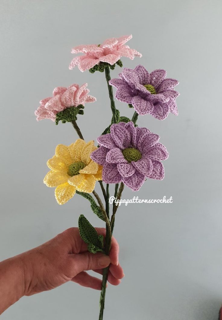 crocheted flowers are being held in the palm of someone's hand on a gray background