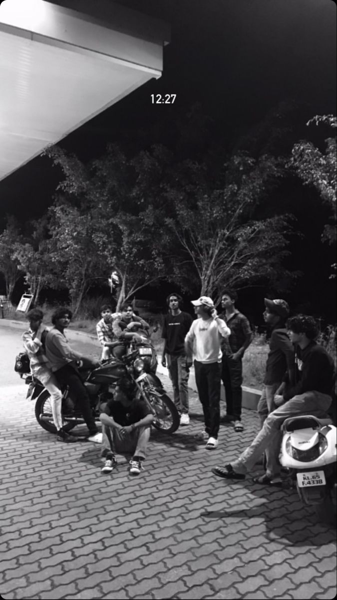 black and white photograph of people sitting on the sidewalk near a gas station at night