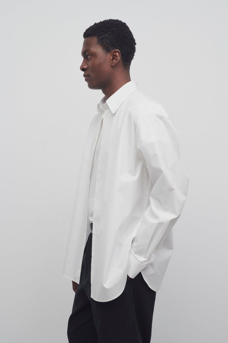 Tailored button-down shirt in woven cotton poplin with exposed placket, horn button closure, and curved hem. Oversized Collared Shirt For Formal Occasions, Modern Button-up Shirt For Daywear, Oversized Business Shirt With Button Closure, Classic Formal Poplin Blouse, Formal Button-up Poplin Tops, Formal Poplin Button-up Top, Oversized Cotton Blouse For Formal Occasions, Modern Button-up Dress Shirt, Modern Button-up Dress Shirt For Daywear