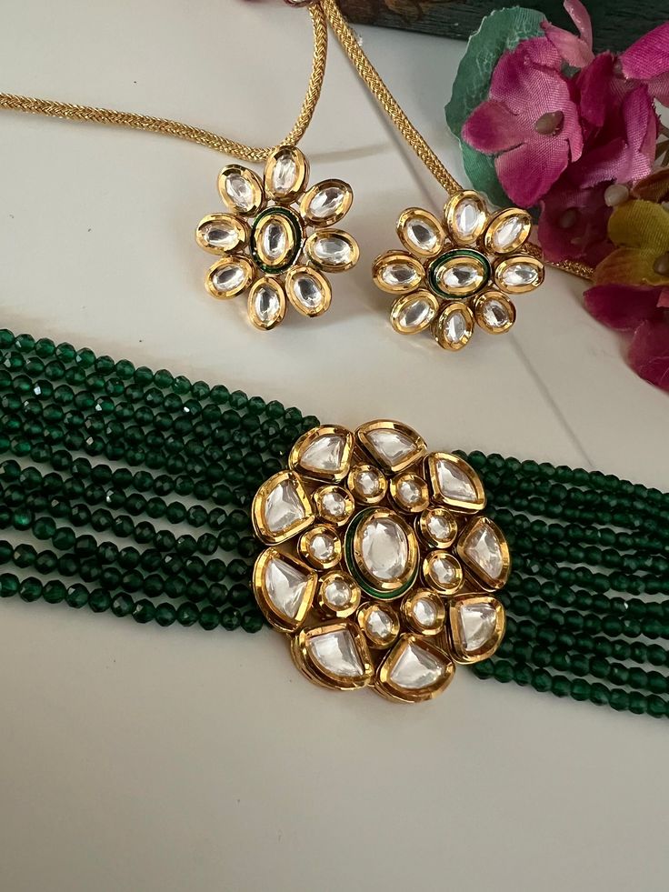 Discover the epitome of elegance with our premium necklace set. Crafted with precision and designed to turn heads, this set is a true masterpiece. Product Details: Material: Each piece is meticulously handcrafted from high-quality brass, Copper, Silver, Kundan Work, Green Beads, Premium Dori. Choker Necklace Dimensions: Weight: 55 grams. Closure Type: Premium Dori Adjustable Size: Yes Width of Choker: 4 cm.  Stud Earring Dimensions (Per Pair): Weight: 16 grams Diameter: 2.8 cm Closure Type: Push Back Closure Exquisite Design: This set boasts a design that's truly captivating, ensuring you stand out on any occasion. Compliment Magnet: Expect a shower of compliments every time you wear this stunning ensemble. Indulge in the finest craftsmanship with our necklace set. Elevate your style, make Elegant Ceremonial Choker, Ceremonial Kundan Jewelry With Elegant Design, Elegant Green Ceremonial Set, Elegant Round Gold Plated Kundan Necklace, Elegant Brass Necklace With Hand Set Details, Elegant Hand Set Brass Necklace, Elegant Brass Necklace With Hand Set, Elegant Hand Set Brass Jewelry, Elegant Hand Set Choker For Ceremonial Use