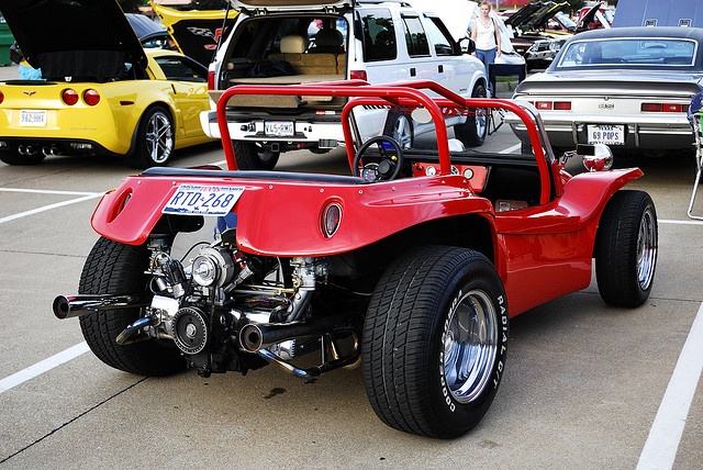 a red four wheeled vehicle parked in a parking lot next to other cars and trucks