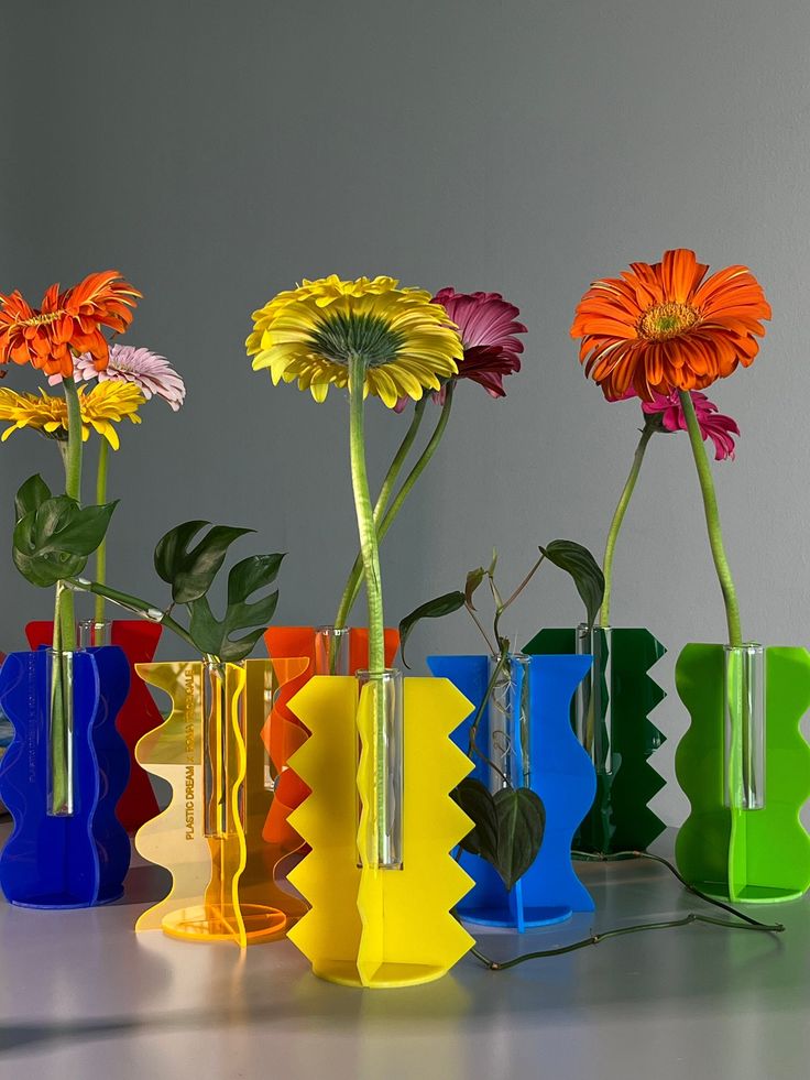 colorful vases with flowers in them sitting on a counter top next to each other