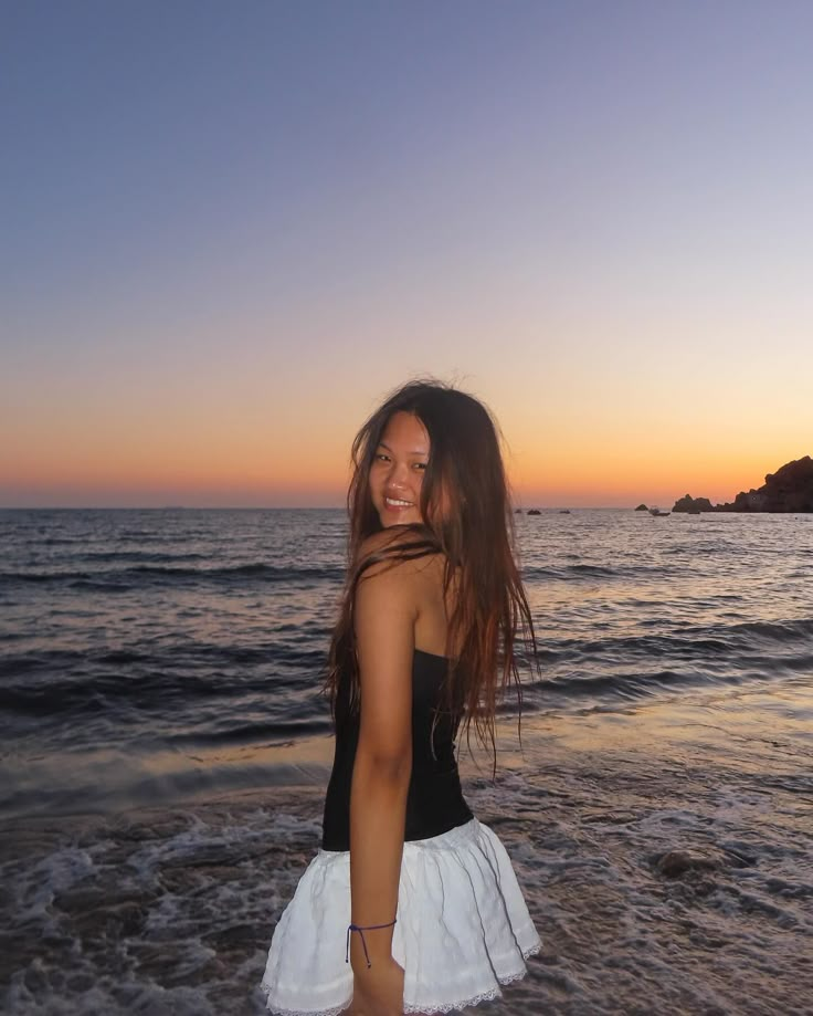 a woman standing on top of a sandy beach next to the ocean at sun set