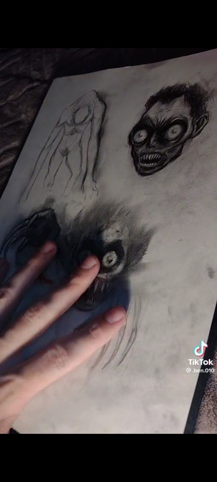 someone is drawing on paper with their hand and skull in the background, while another person's hands are next to them