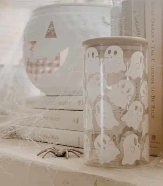 a stack of books sitting on top of a shelf next to a glass cup with ghost stickers on it