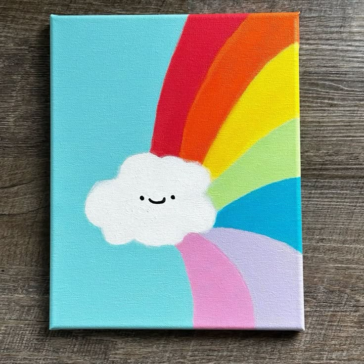 a painting of a rainbow with a smiling cloud on it's face, sitting on top of a wooden table