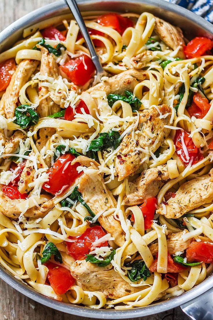 a skillet filled with chicken, tomato and spinach pasta on top of a wooden table