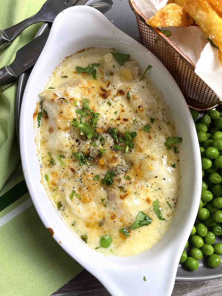 a white bowl filled with food next to green peas and bread on top of a table