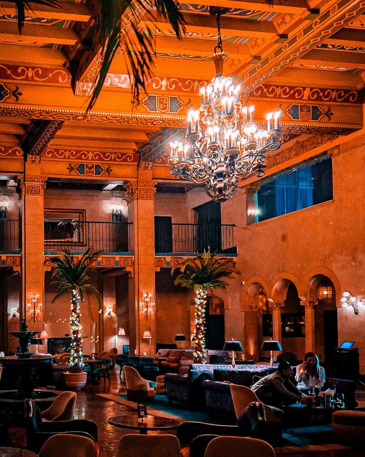 a large room with chandeliers and couches in the center, surrounded by palm trees