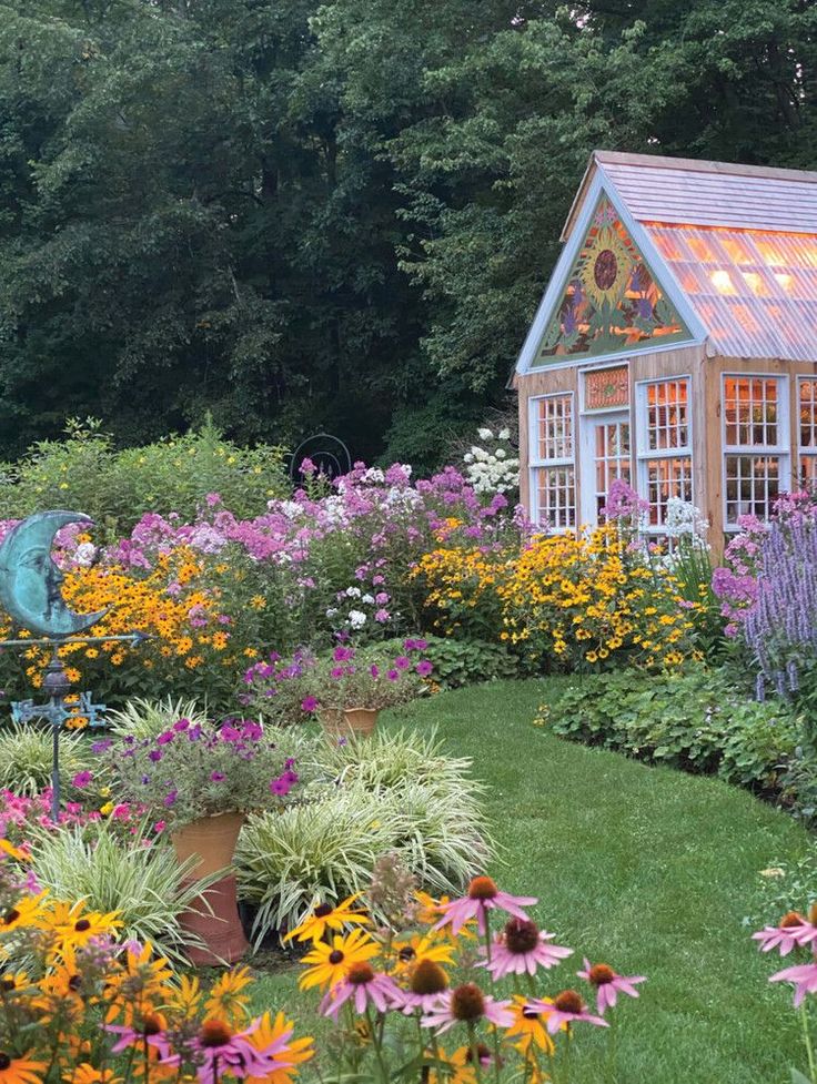 a garden filled with lots of flowers next to a small wooden house on top of a lush green field