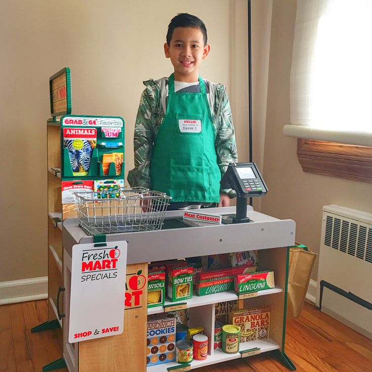 a young boy in an apron standing behind a food stand