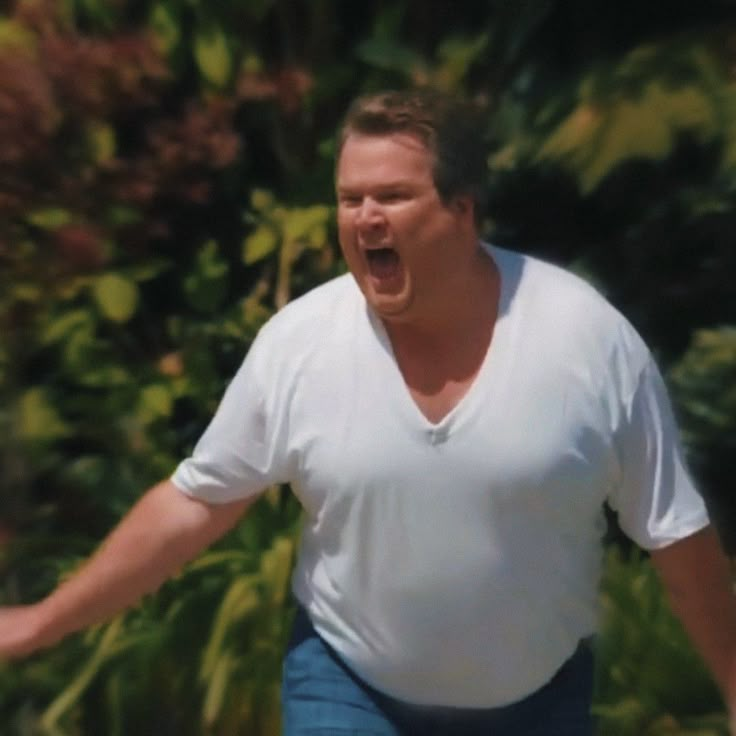 a man in white shirt and blue pants holding a frisbee with his mouth open