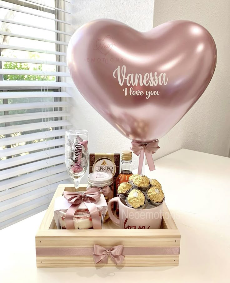 a pink heart shaped balloon sitting on top of a wooden box filled with chocolates