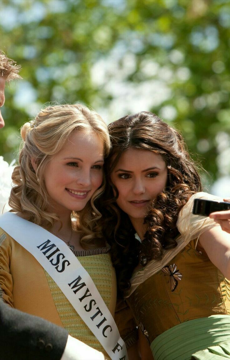 two young women taking a selfie with a man in the background wearing a miss america sash