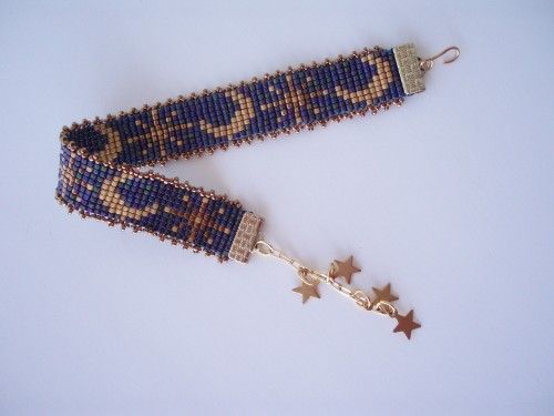 a blue and gold beaded bracelet with stars hanging from it's side on a white surface