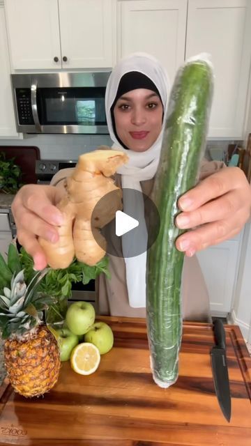 a woman is holding cucumbers on a cutting board in front of some fruits and vegetables