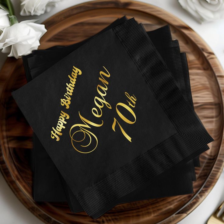 three black napkins with gold lettering on them sitting on top of a wooden plate