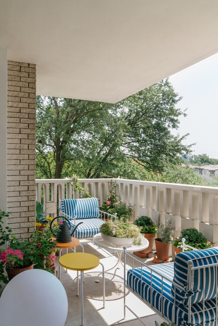 a balcony with blue and white striped chairs, potted plants, and yellow table