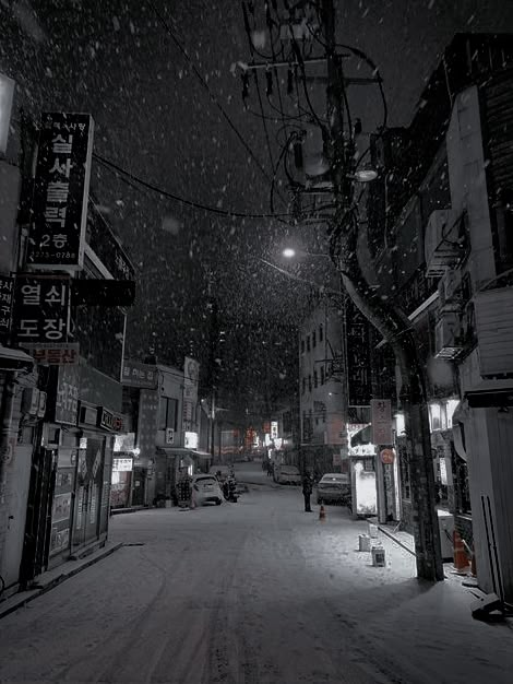 a snowy street at night with cars parked on the side and people walking down it