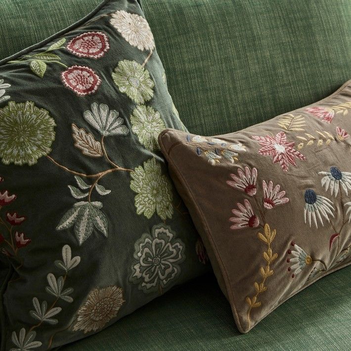 two pillows are sitting on the back of a green couch, one has a floral design