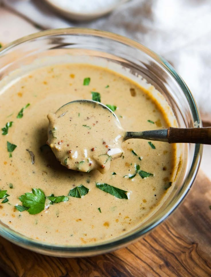 a glass bowl filled with soup on top of a wooden cutting board next to a spoon