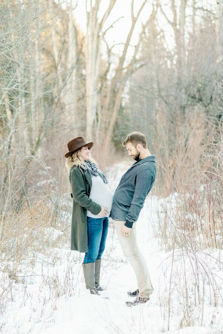 a pregnant woman standing next to a man in the snow