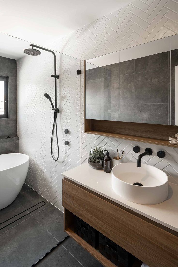 this gorgeous bathroom features white herringbone tiles that are complimented by the warmth of the wooden vanity. The dark tiles and matte black tapware add a contrast to the otherwise bright bathroom Bathroom White And Grey Tiles, Colour Bathroom Vanity, Bathroom Tile Ideas Dark Floor, Bathroom Grey Tiles White Walls, Bathroom Grey White Wood, Contrasting Tiles Bathroom, Small Bathroom Ideas Dark Floor, Black White Grey Wood Bathroom, Dark Flooring Bathroom Ideas