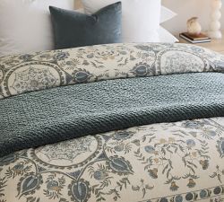 a bed with blue and white comforter on top of it next to a night stand