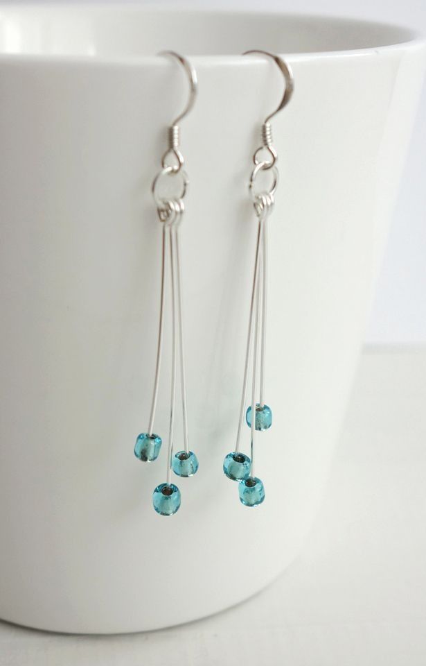 some kind of earrings with blue beads hanging from it's earwires on a white cup