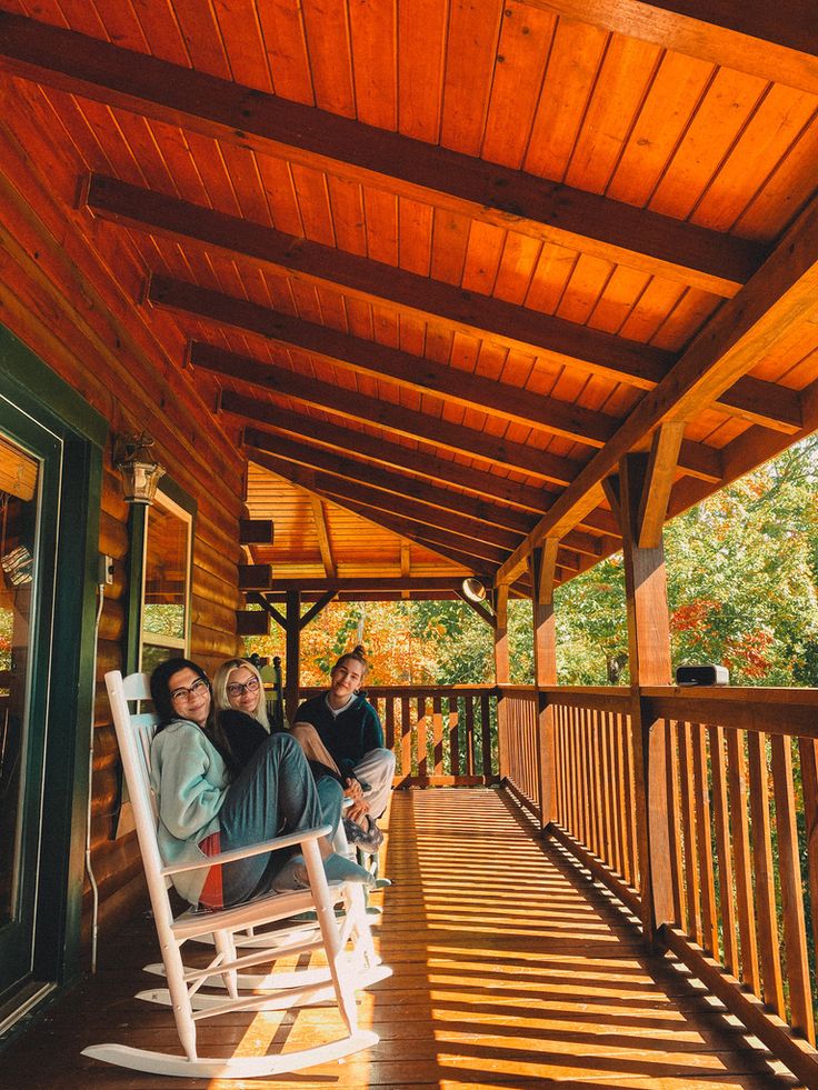 two people sitting on a rocking chair on a porch with wood planked ceilinging