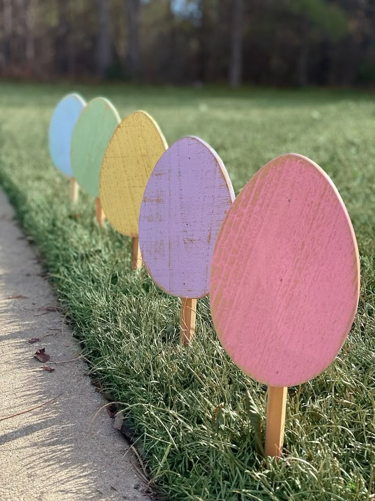 four wooden easter eggs are lined up on the grass in front of a sidewalk and trees