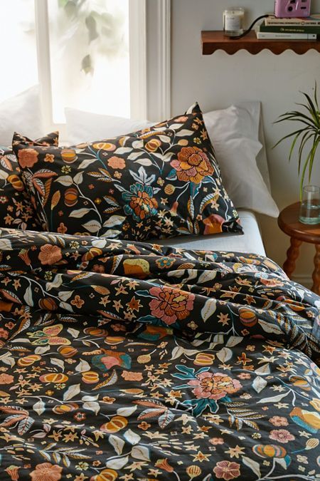 a bed with black and orange flowers on it, in front of a large window