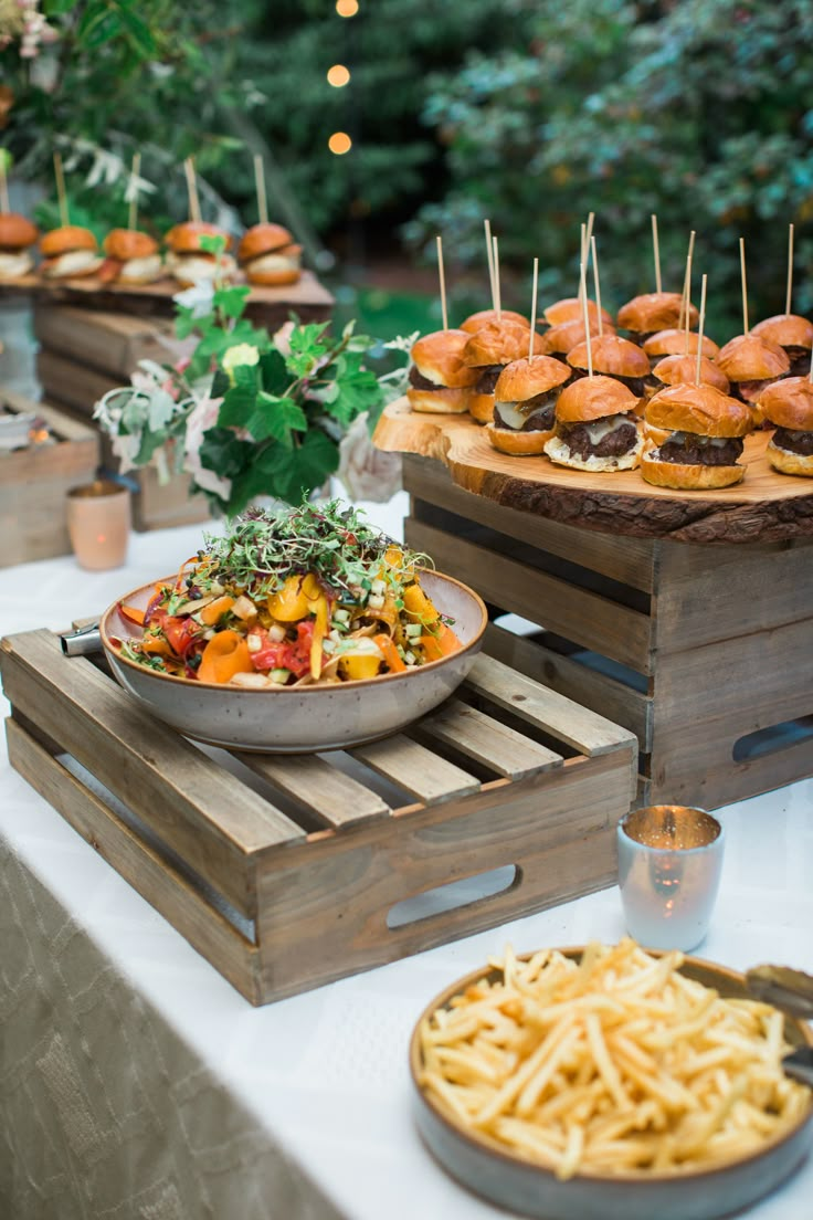 a table topped with plates of food next to wooden trays filled with burgers