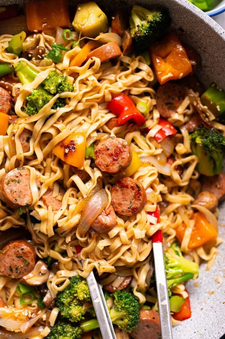 a bowl filled with noodles, sausage and veggies next to broccoli