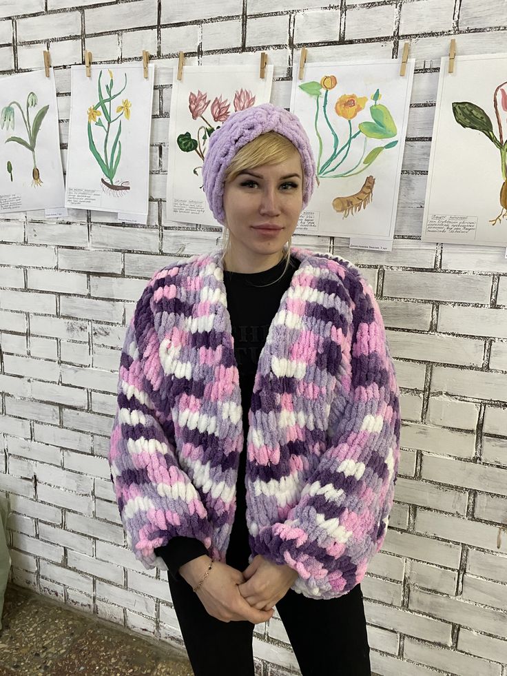 a woman standing in front of a brick wall wearing a knitted sweater and hat