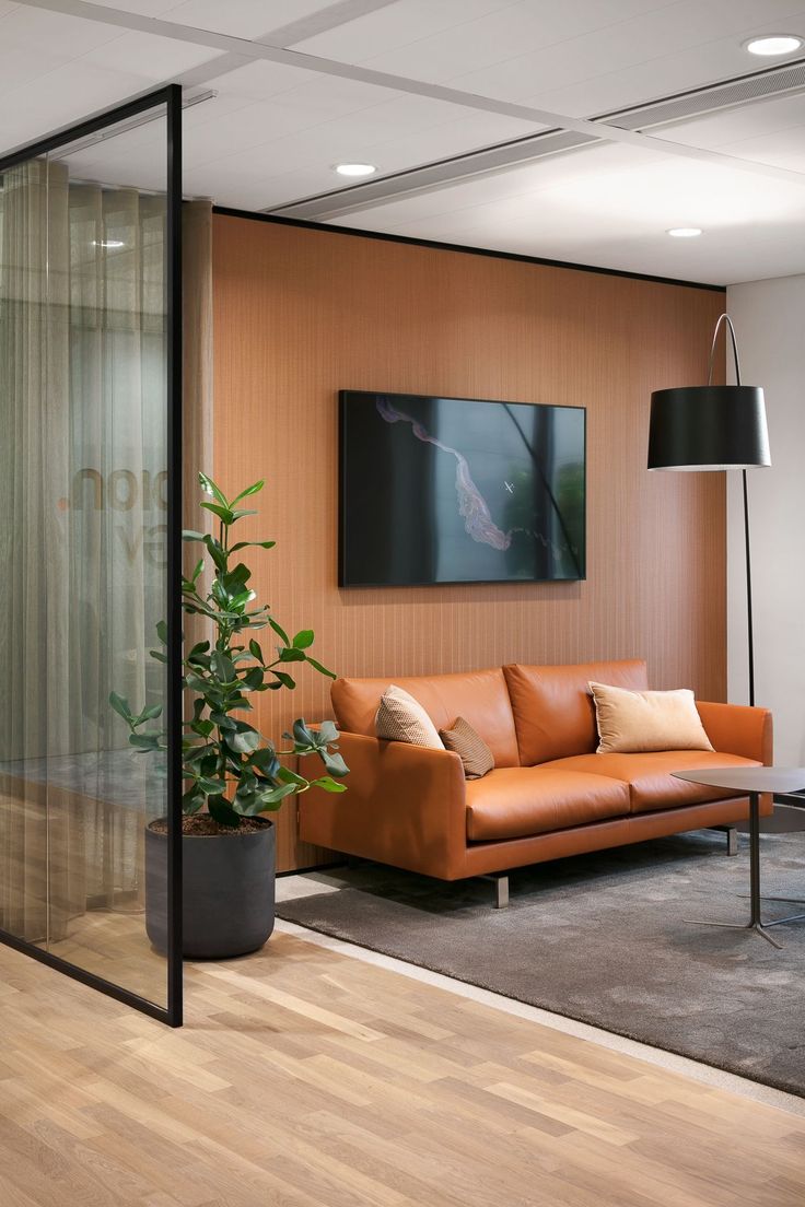 a living room with a couch, chair and plant in front of a glass wall