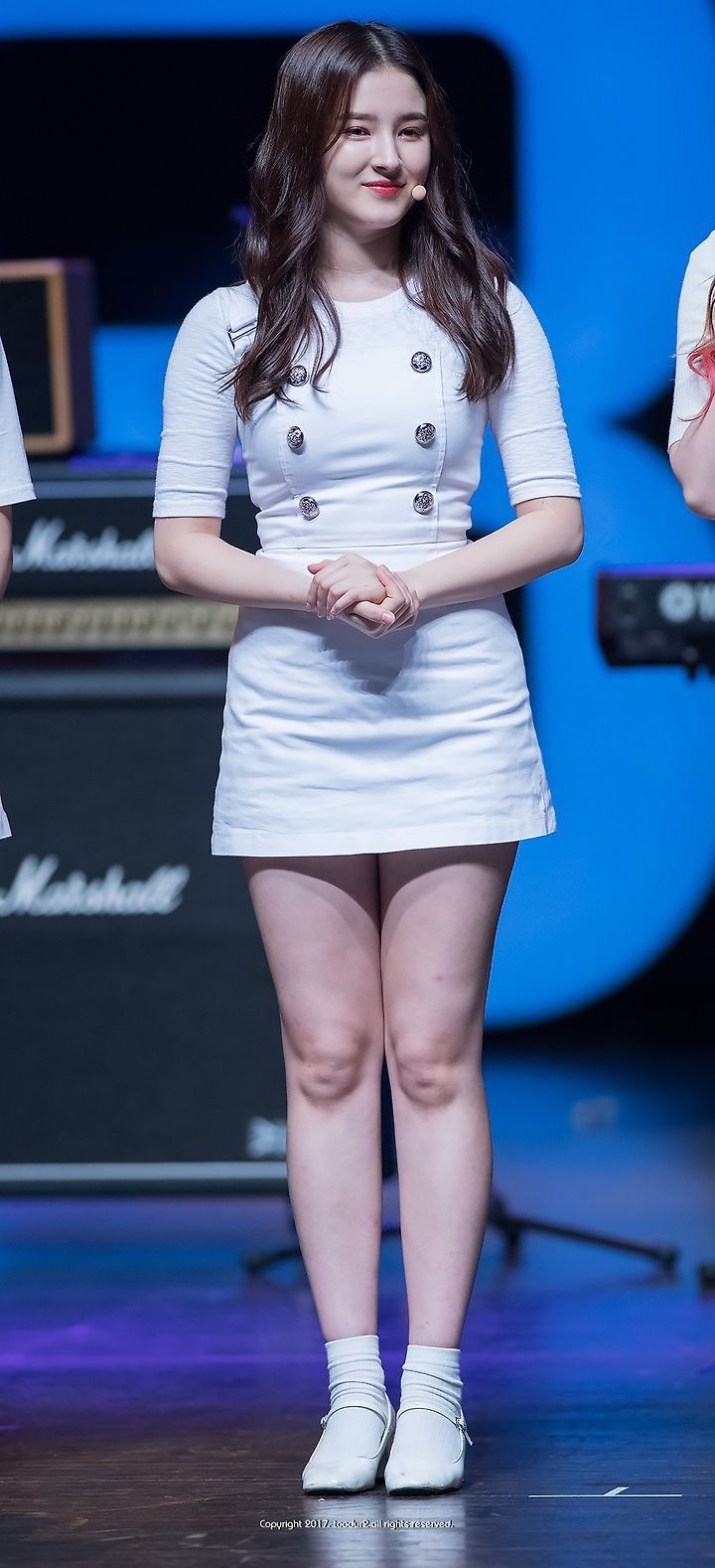 a woman in white dress standing on stage with her hands folded over her chest and looking at the camera