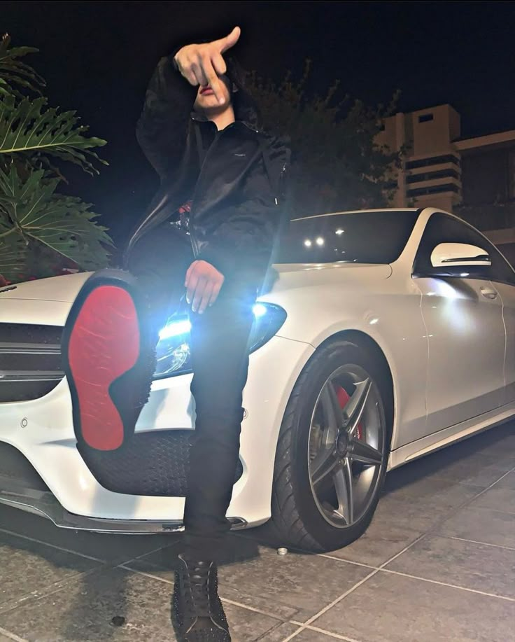 a man sitting on the hood of a white car with his hand up in the air