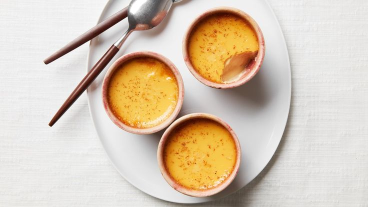 three small bowls filled with soup on top of a white plate next to two spoons