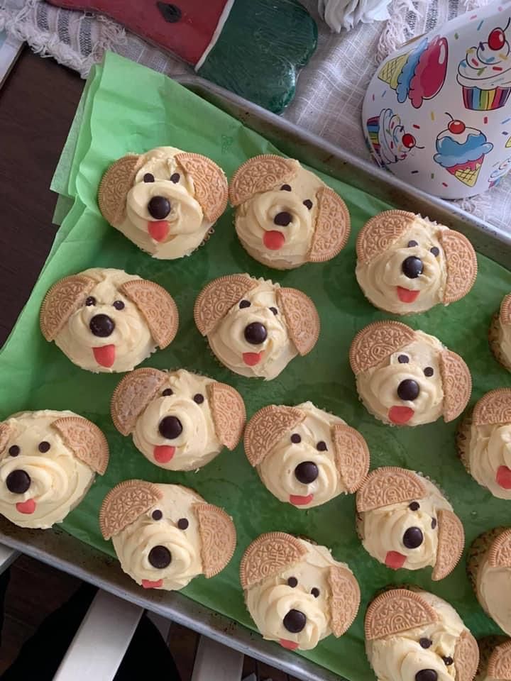 cupcakes with frosting and dog faces are on a green tray next to a balloon